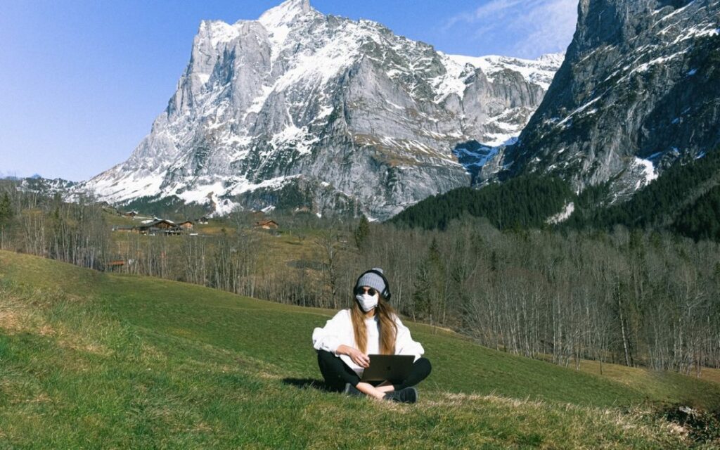 woman wearing a face mask working on her computer in front of a snow-capped mountain